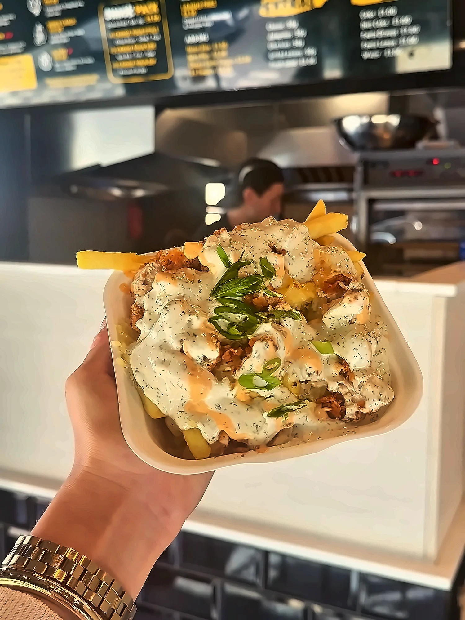 Loaded fries held up in the shop: fries topped with chopped chicken, cheese, ranch and red pepper mayo