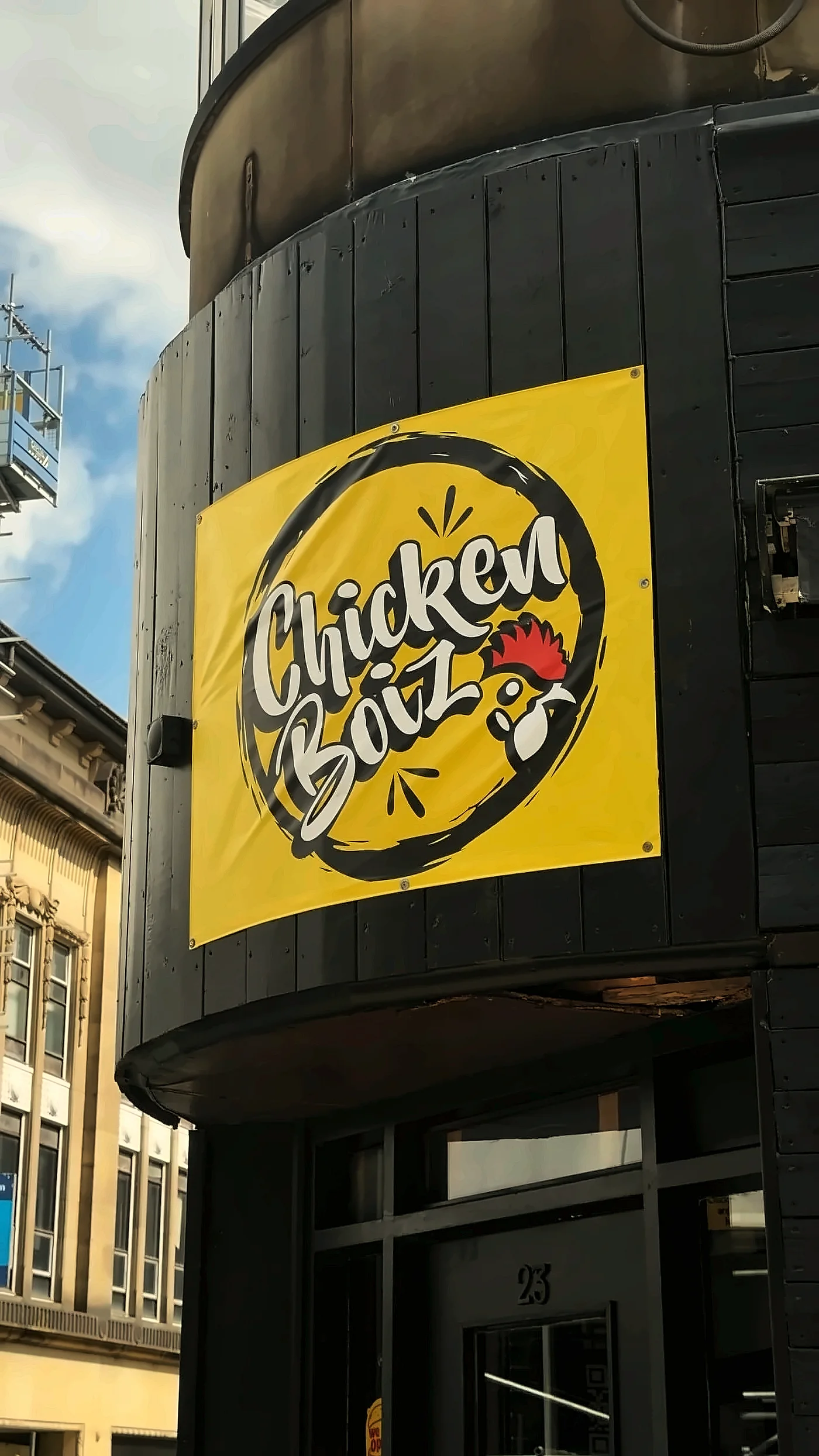 The Chicken Boiz shopfront: black cladding with the yellow Chicken Boiz sign on the corner of the building