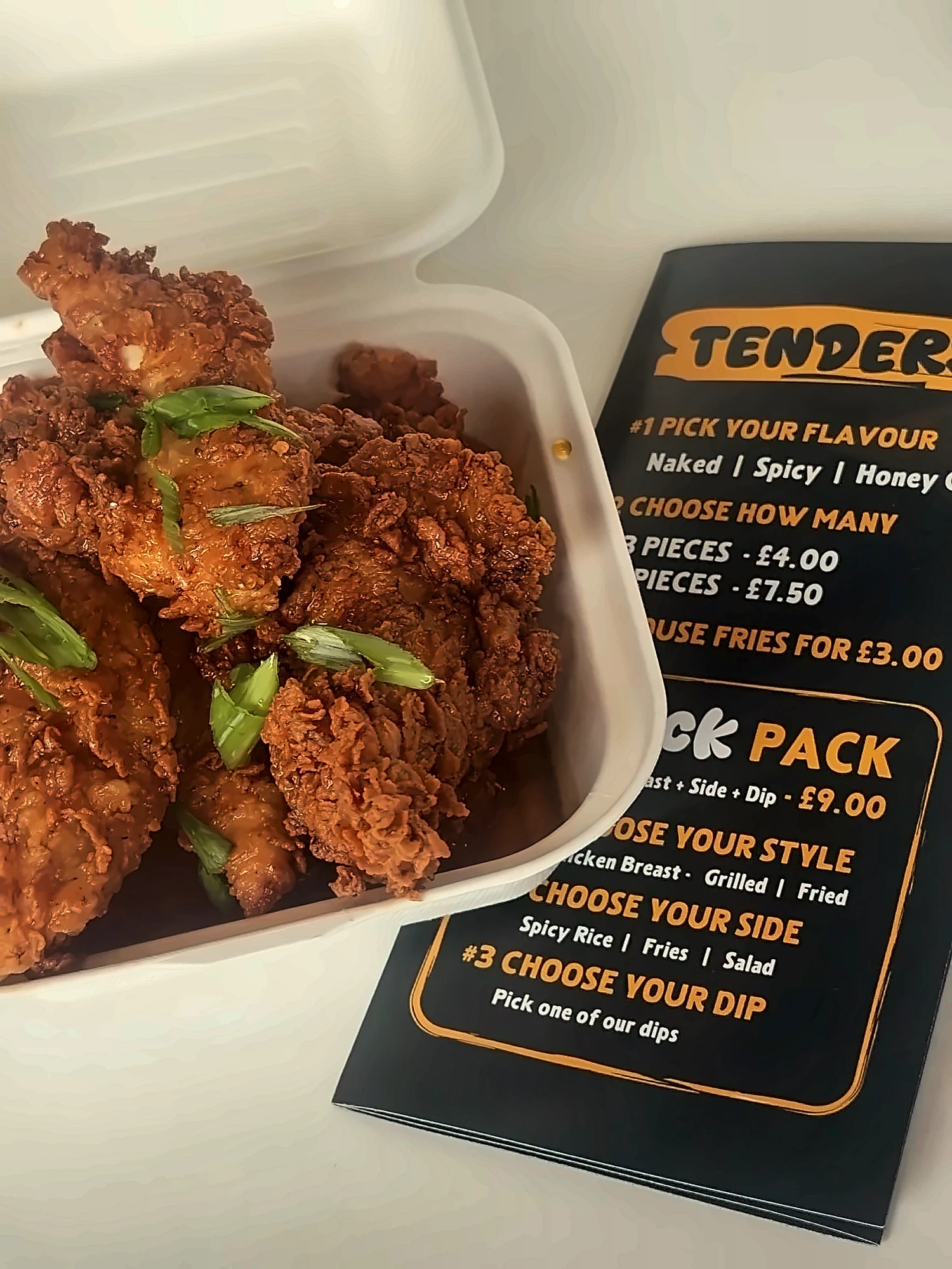 Honey garlic chicken tenders topped with spring onions, in a takeaway box next to the Chicken Boiz tenders menu